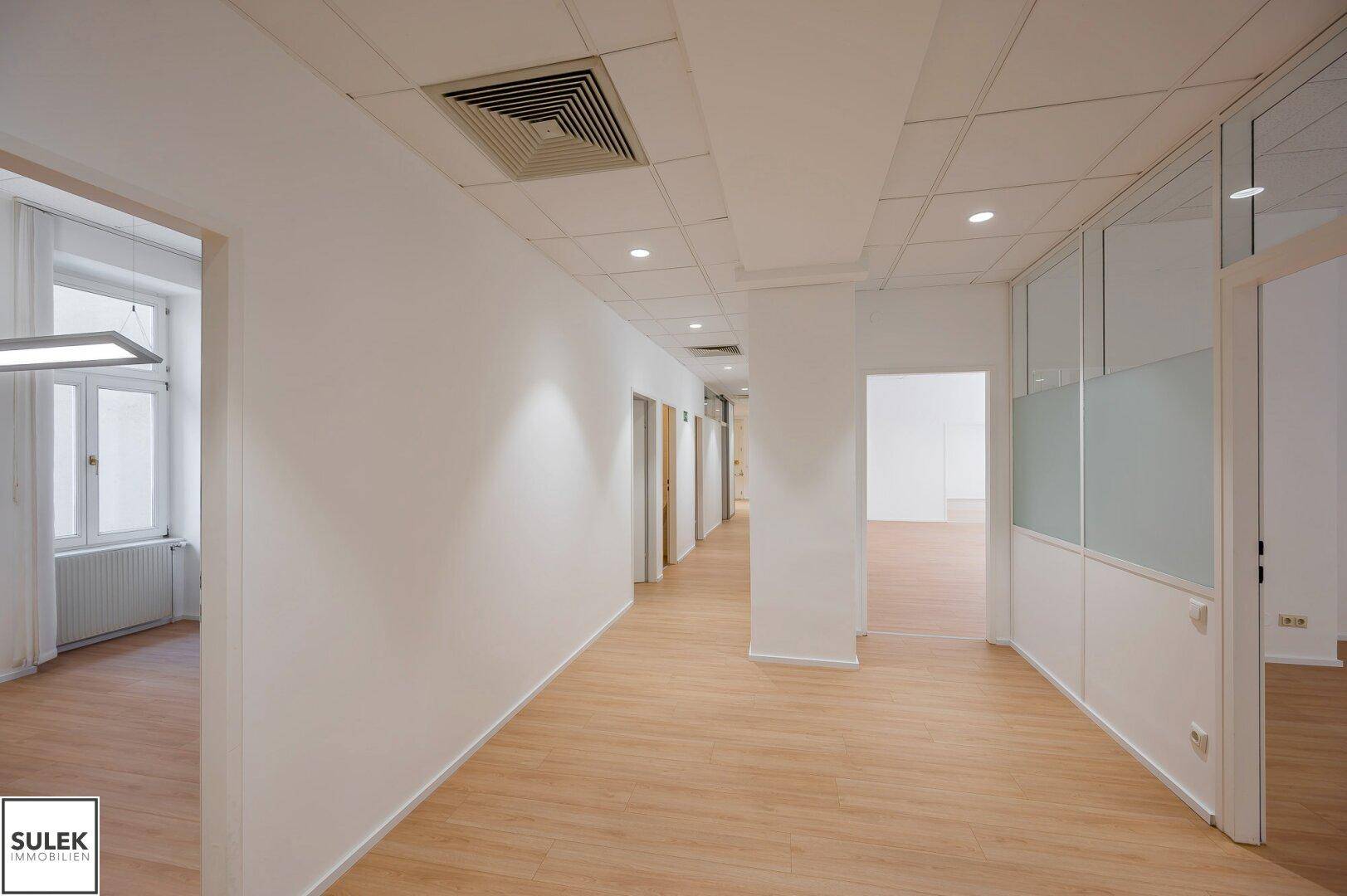 Langer, heller Bürogang mit abgehängter Decke und Einbaustrahlern, der mehrere Türen verbindet.