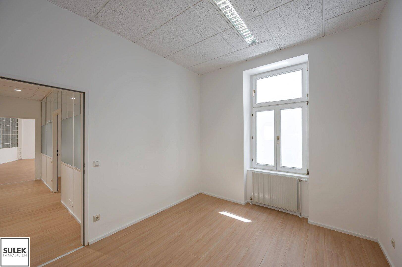 Kleineres Büro mit einem großen Fenster, das viel Tageslicht hereinlässt, und hellem Laminatboden.