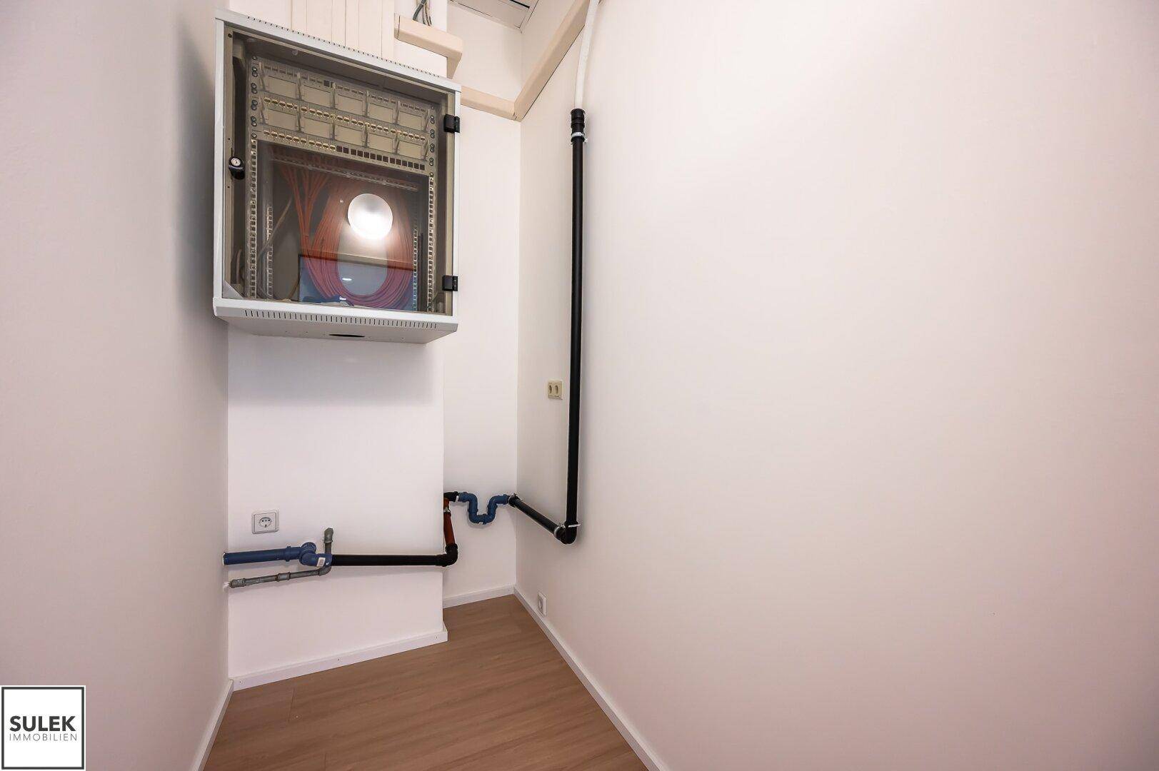 Kleiner Abstellraum mit einem Verteilerkasten und sichtbaren Rohren an der Wand.
