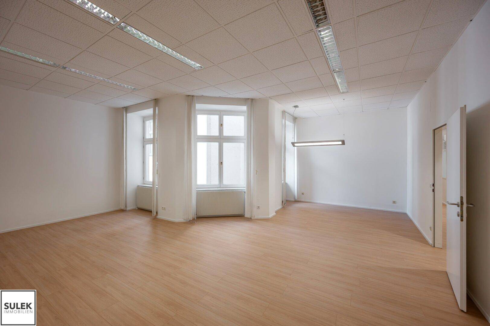 Großes, helles Büro mit mehreren Fenstern, die viel Tageslicht hereinlassen, und hellem Laminatboden.