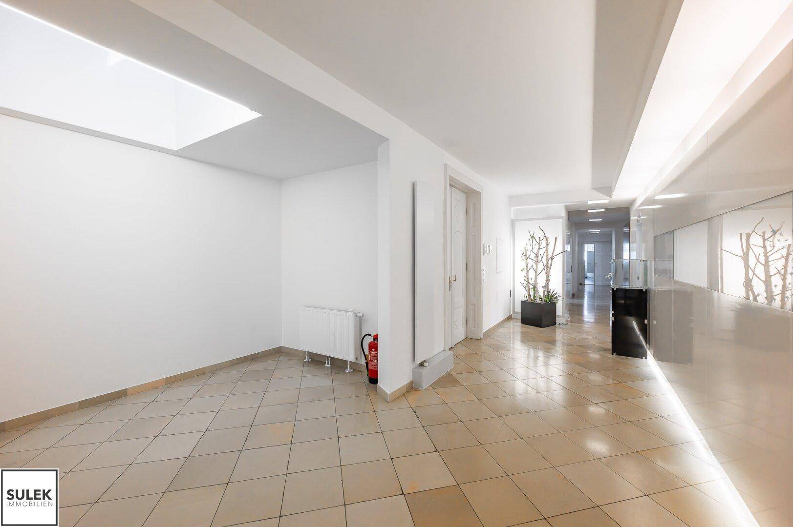 Geräumiger Flur mit Fliesenboden, Oberlicht und einem Feuerlöscher an der Wand.