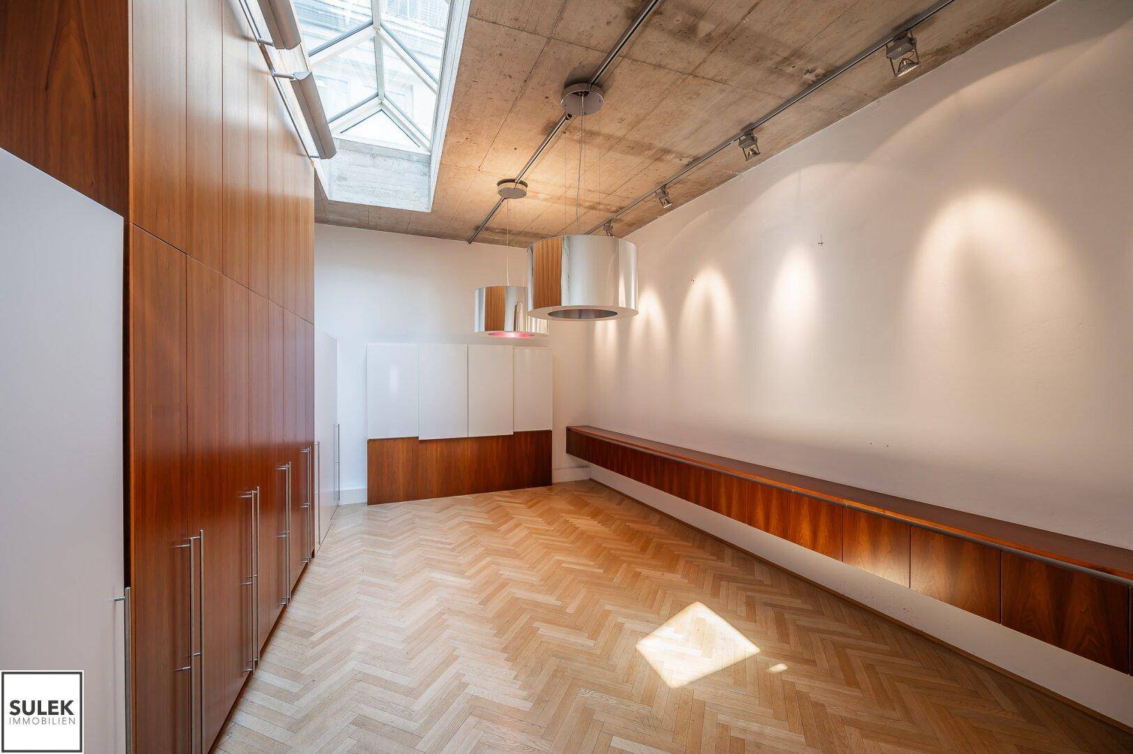 Modernes Büro mit Fischgrätparkett, Holzschränken und einer Betondecke mit Oberlicht.