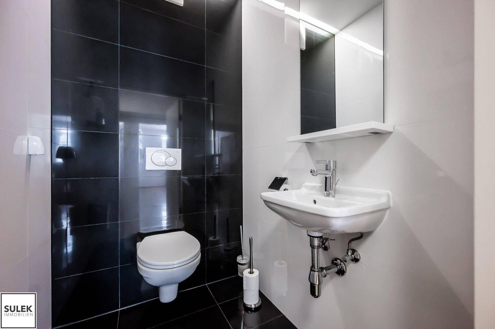 Stilvolles Badezimmer mit schwarzen und weißen Fliesen, ausgestattet mit WC und modernem Waschbecken.