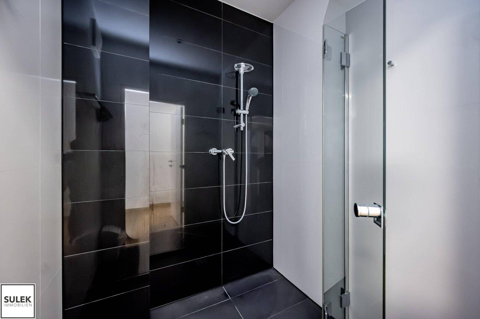 Moderne Duschkabine mit schwarzen Hochglanzfliesen und einer eleganten Glasabtrennung.