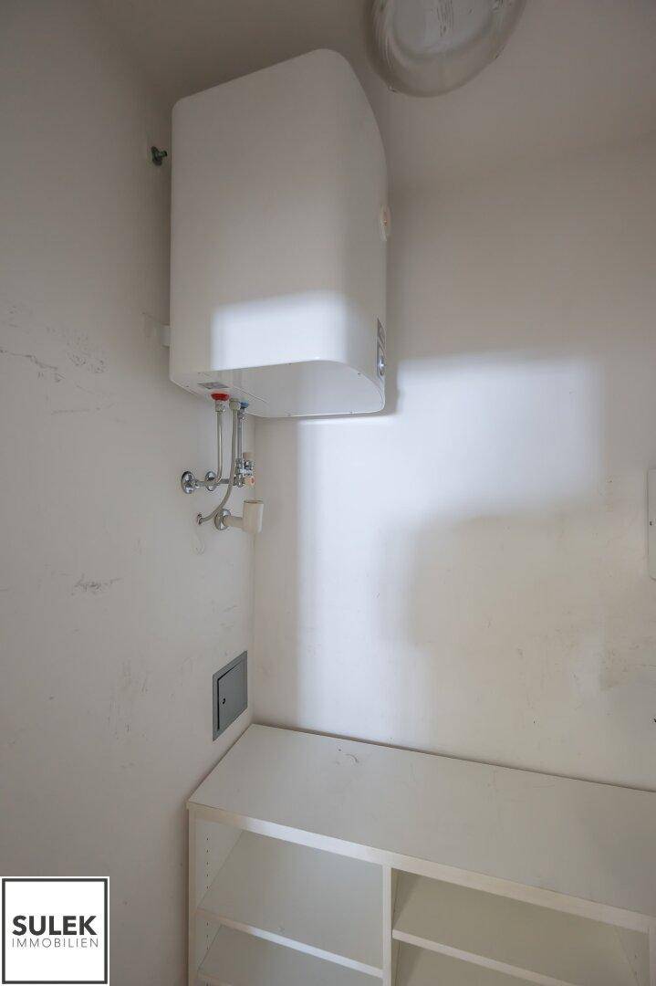 Kleiner Abstellraum mit Warmwasserbereiter an der Wand und einfachen Regalen.