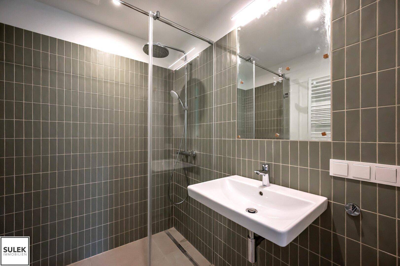 Modernes Badezimmer mit ebenerdiger Dusche, Einzelwaschbecken und grün-grauen Wandfliesen.
