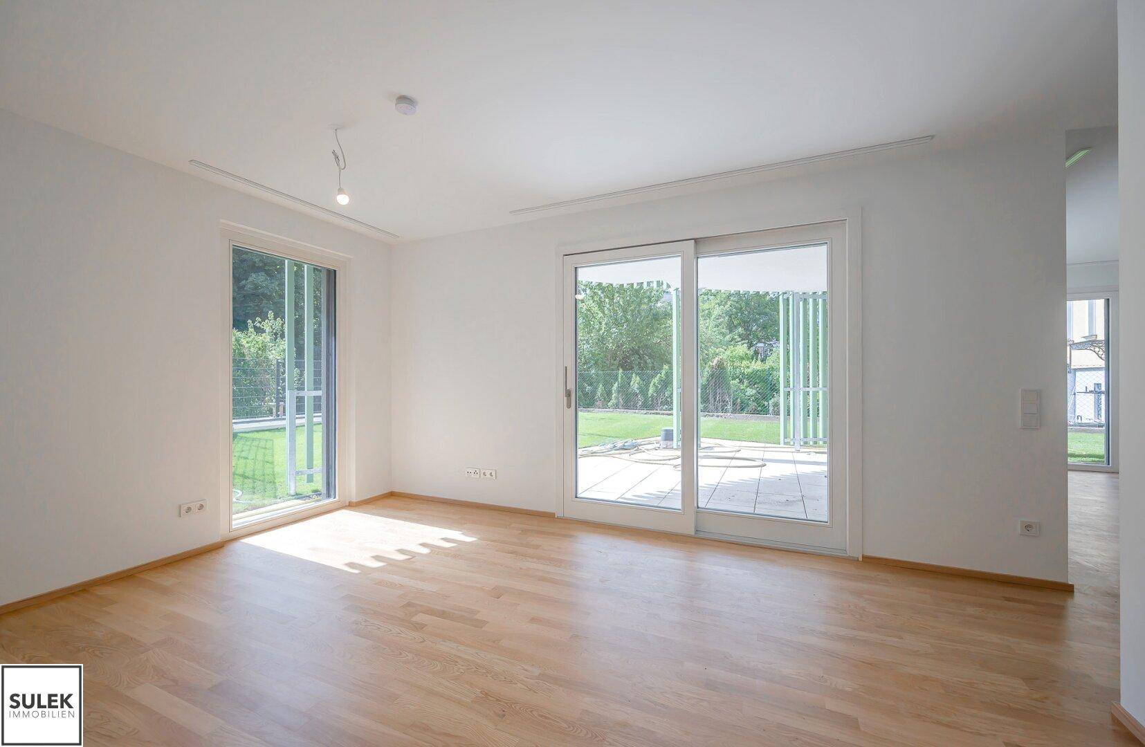 Heller Wohnraum mit Holzboden und großen Fenstern, die viel Tageslicht hereinlassen.
