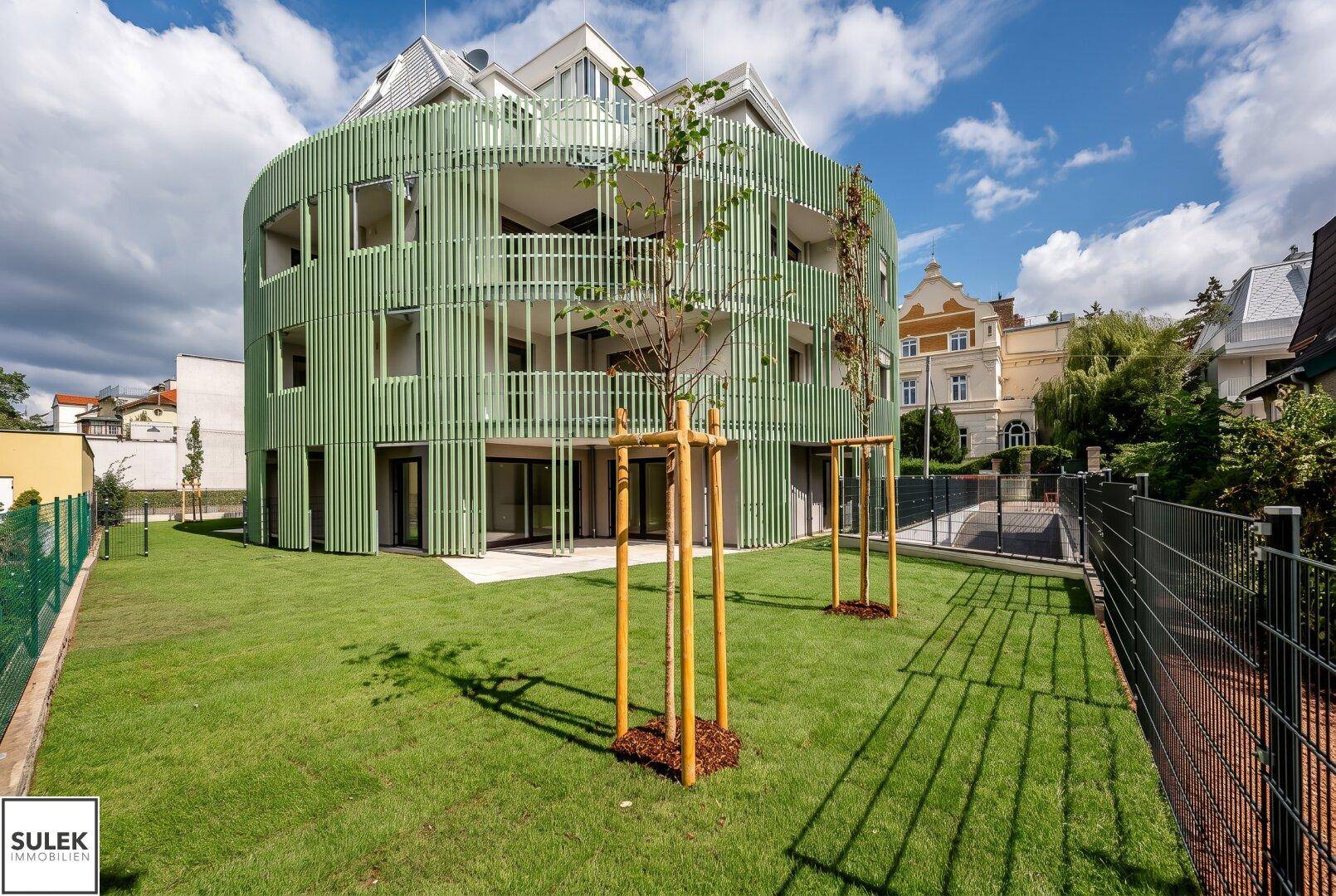 Modernes Mehrfamilienhaus mit auffälliger grüner Fassadenverkleidung und gepflegter Grünanlage.