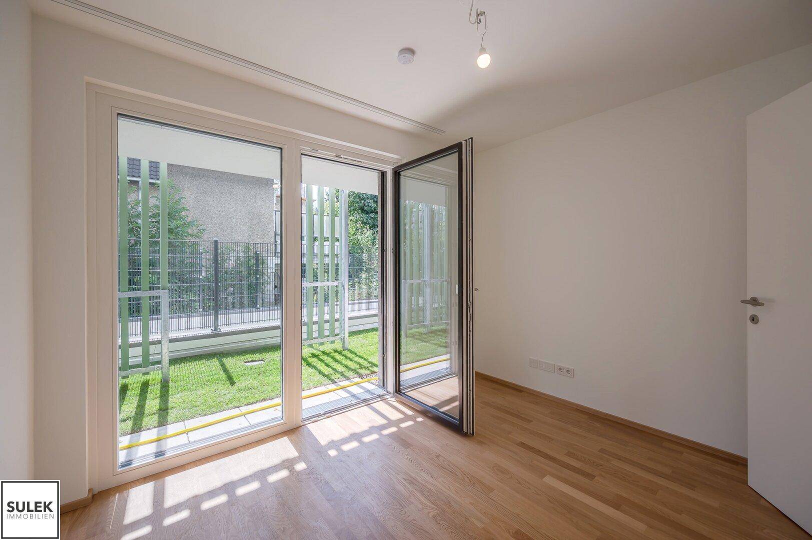 Freundliches Zimmer mit Holzboden und bodentiefen Fenstern, die viel Licht spenden.