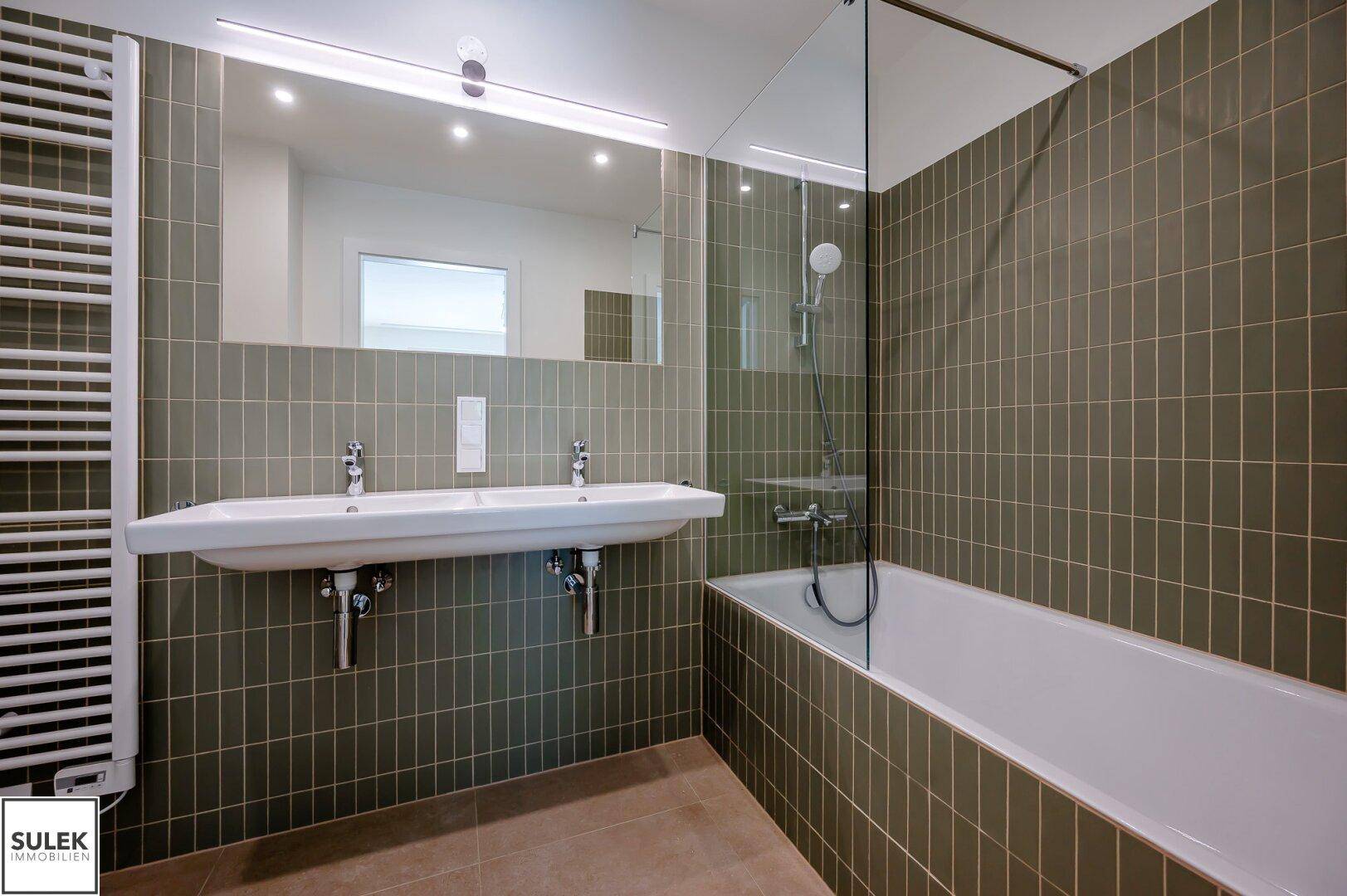 Helles Badezimmer mit Badewanne, Doppelwaschbecken und beheiztem Handtuchhalter.