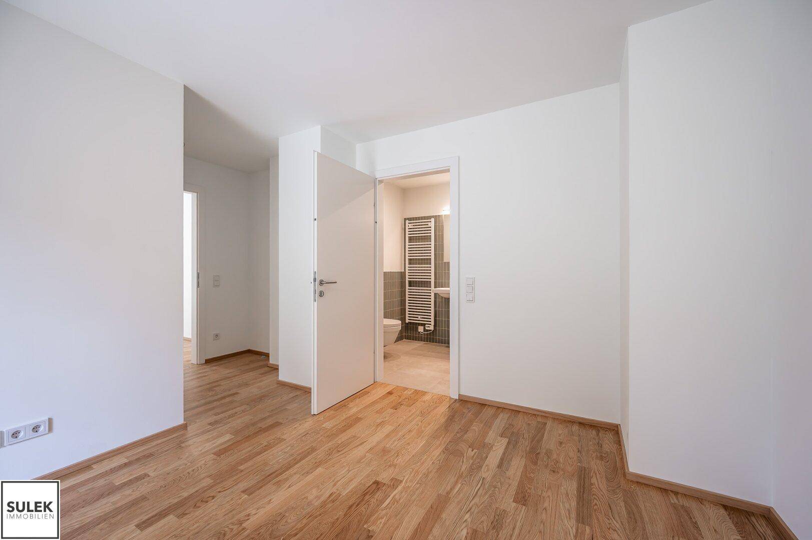 Flur mit Holzboden und Blick in ein angrenzendes Badezimmer.
