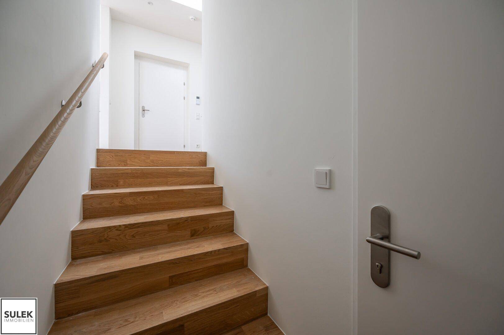 Holztreppe mit Handlauf, die zu einem oberen Stockwerk führt, in einem hellen Flur.