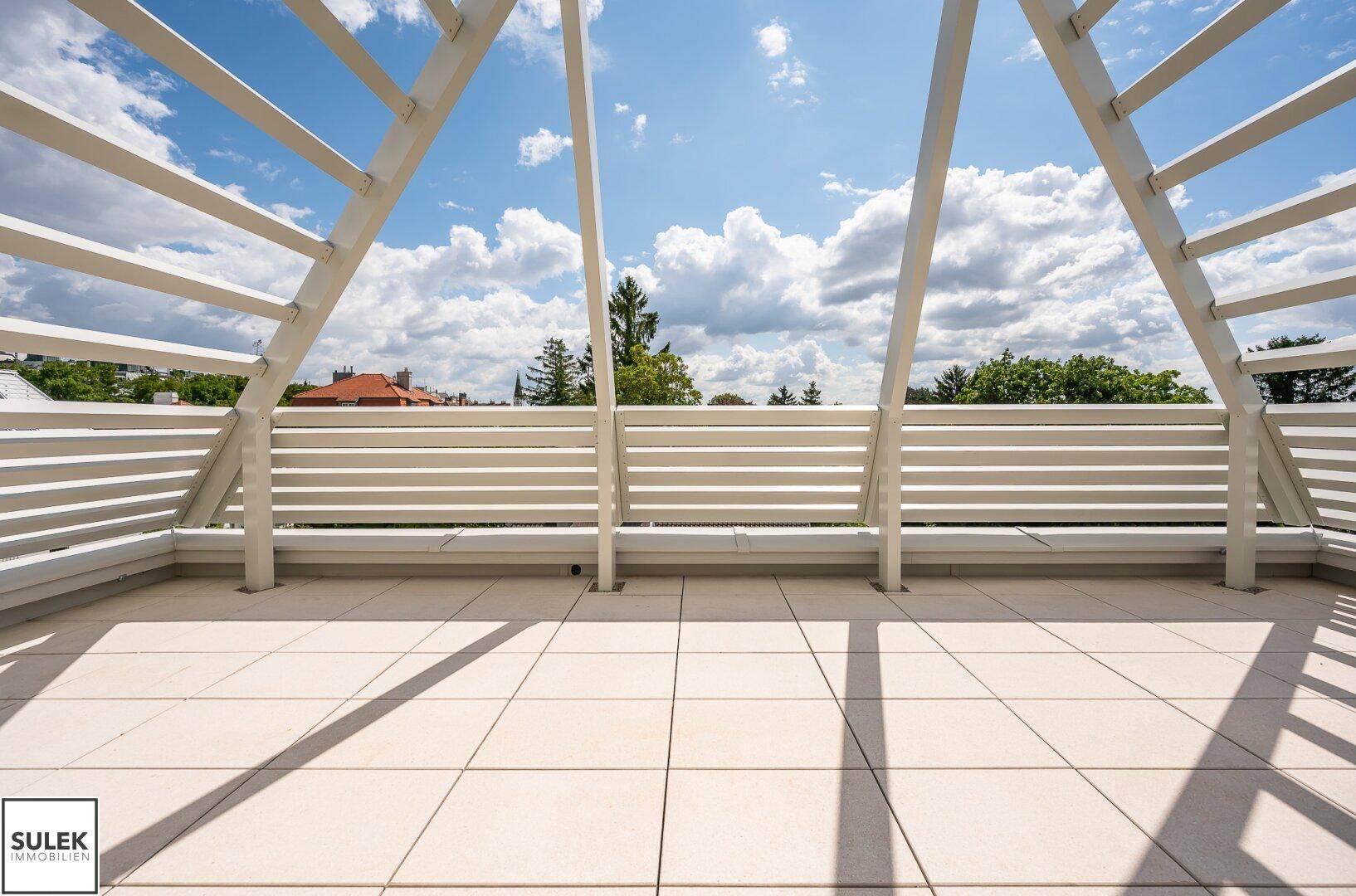 Geräumige Dachterrasse mit modernen weißen Geländern und hellem Fliesenboden unter blauem Himmel.