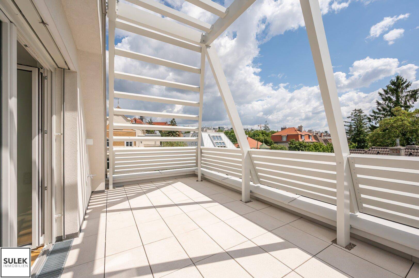 Helle Terrasse mit modernem Design, Fliesenboden und Zugang zu den Innenräumen, umgeben von Grün.