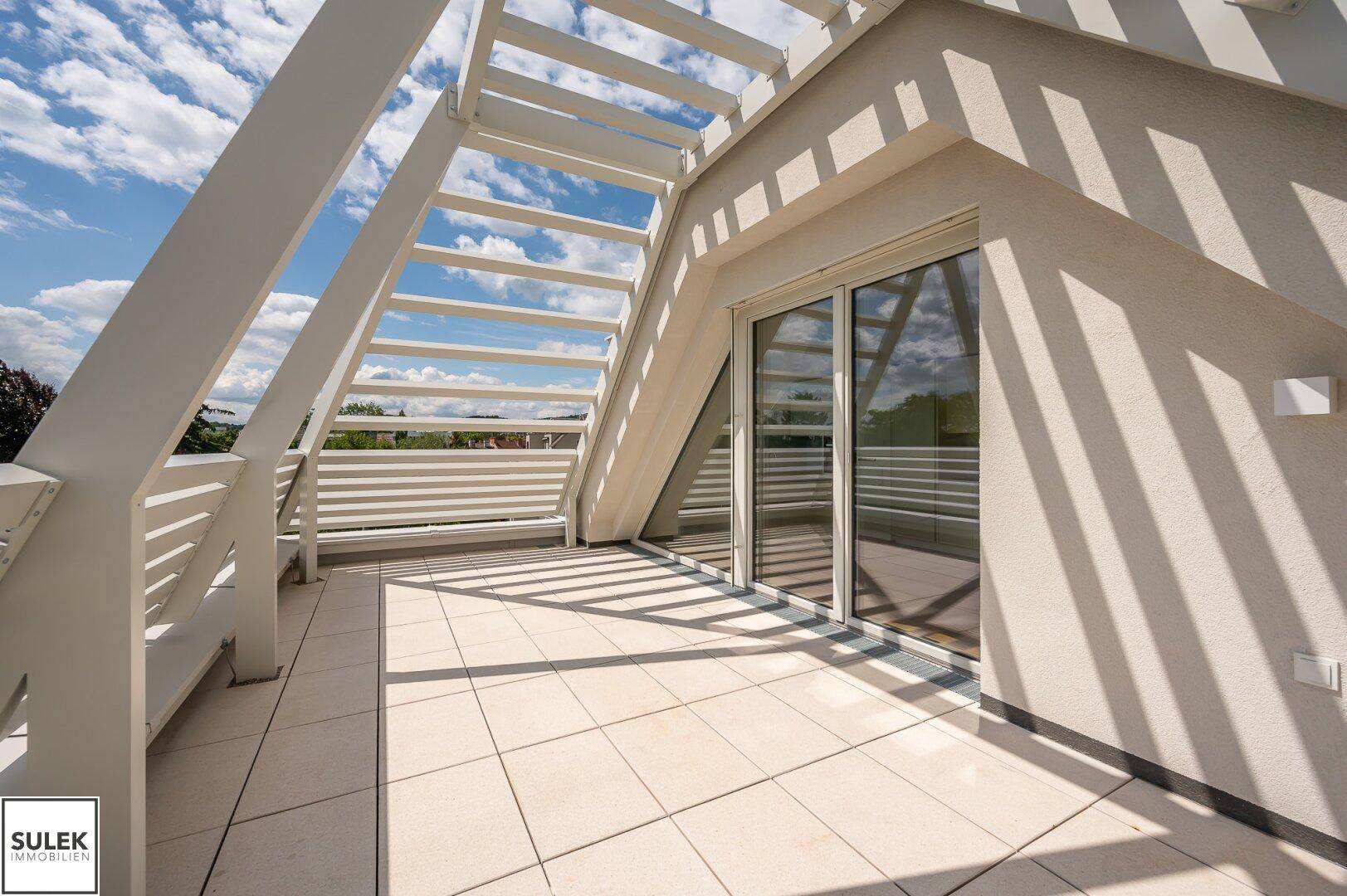 Geräumige Dachterrasse mit Fliesenboden und moderner Geländerkonstruktion unter blauem Himmel.