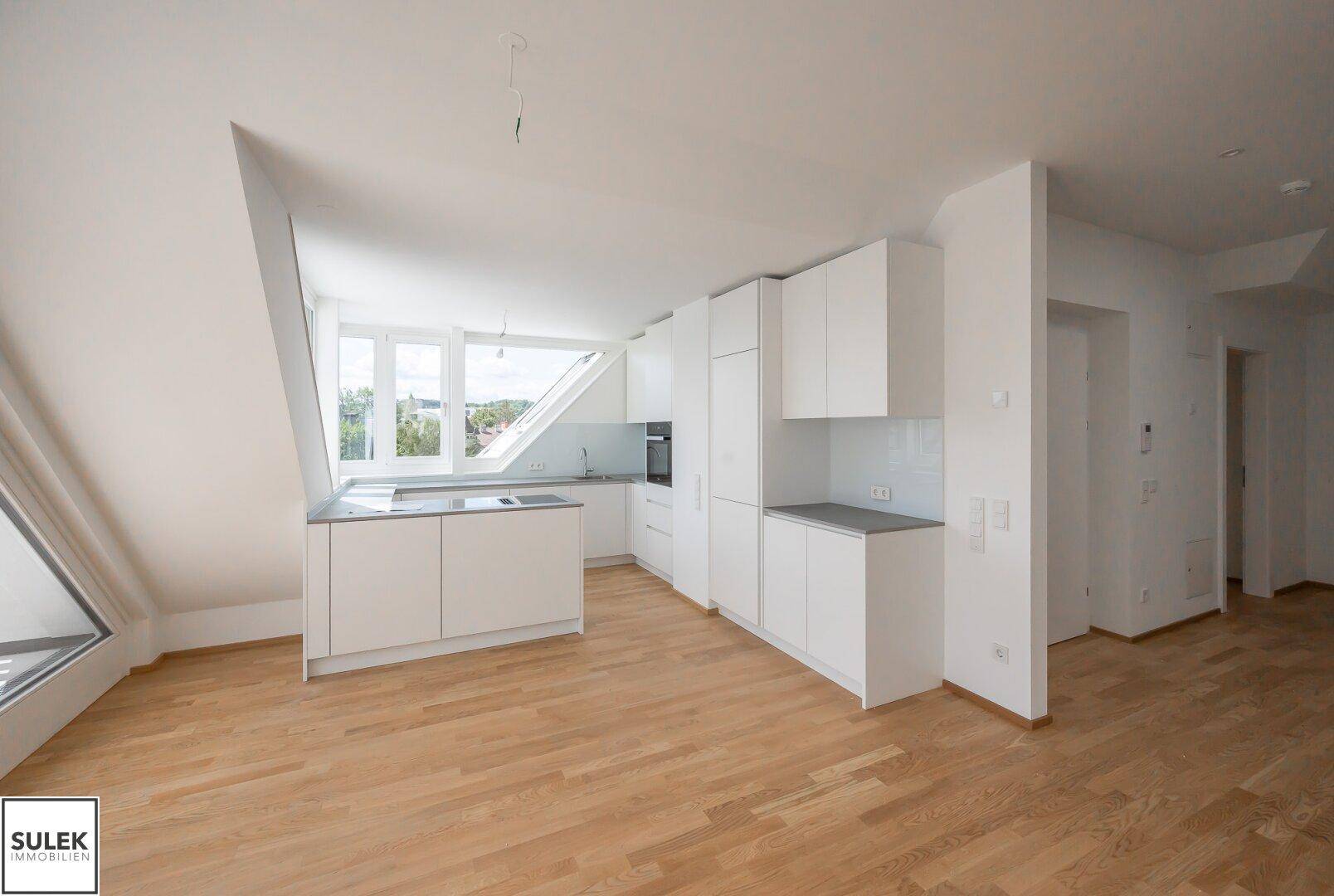Offene Küche mit weißen Schränken, grauer Arbeitsplatte und Holzboden in einem Dachgeschoss.