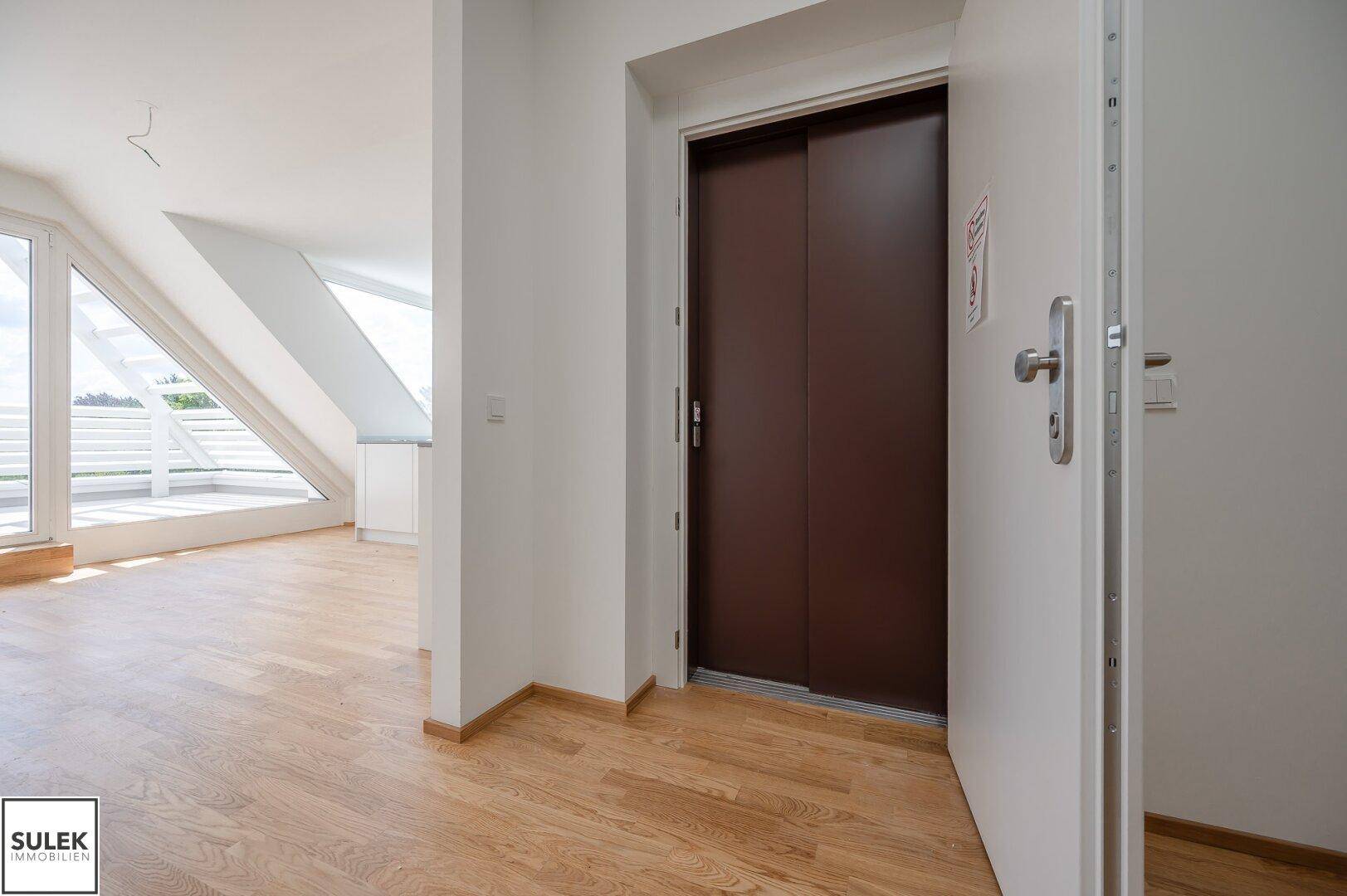 Heller Flur mit Holzboden und Zugang zu einem modernen Aufzug im Gebäude.