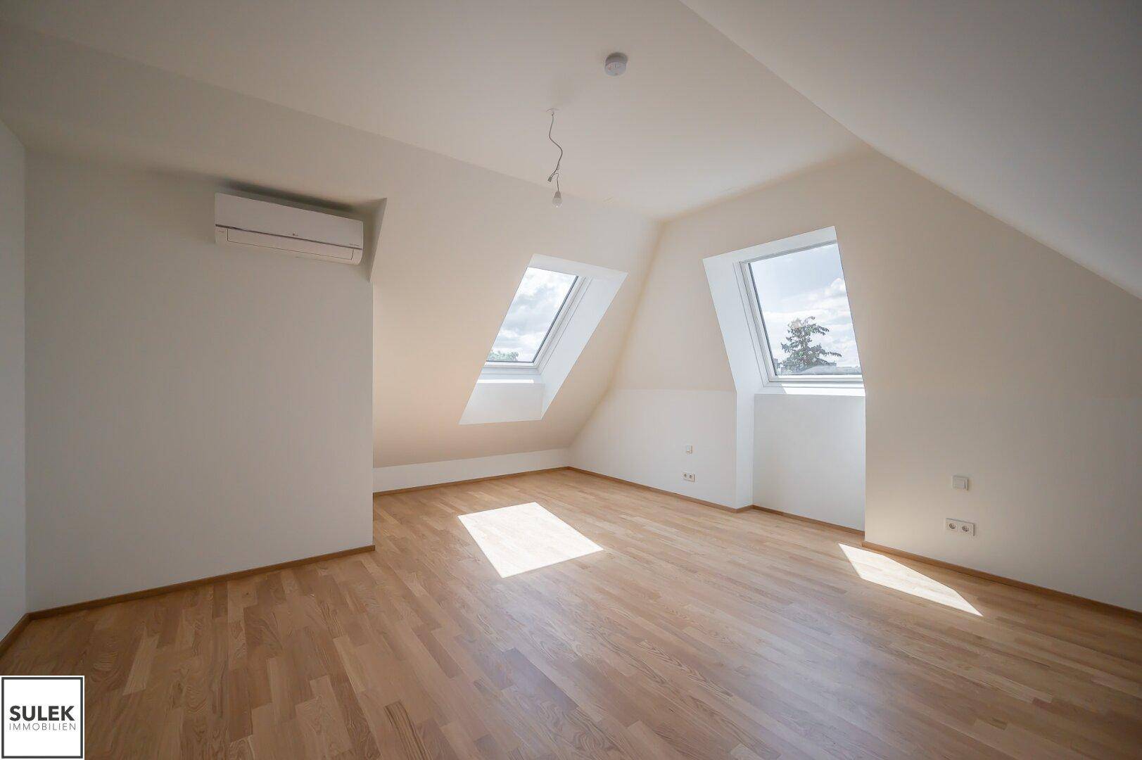 Helles Schlafzimmer im Dachgeschoss mit Holzboden, Dachfenstern und Klimaanlage.