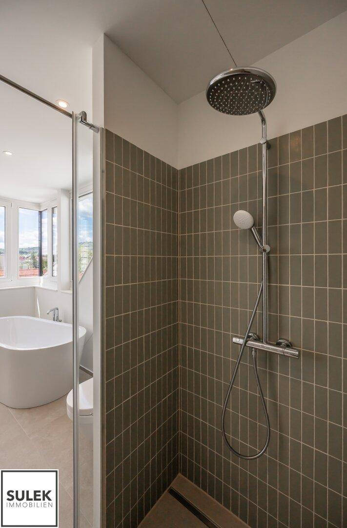 Moderne Dusche mit Regenduschkopf und grauen Fliesen in einem hellen Badezimmer.