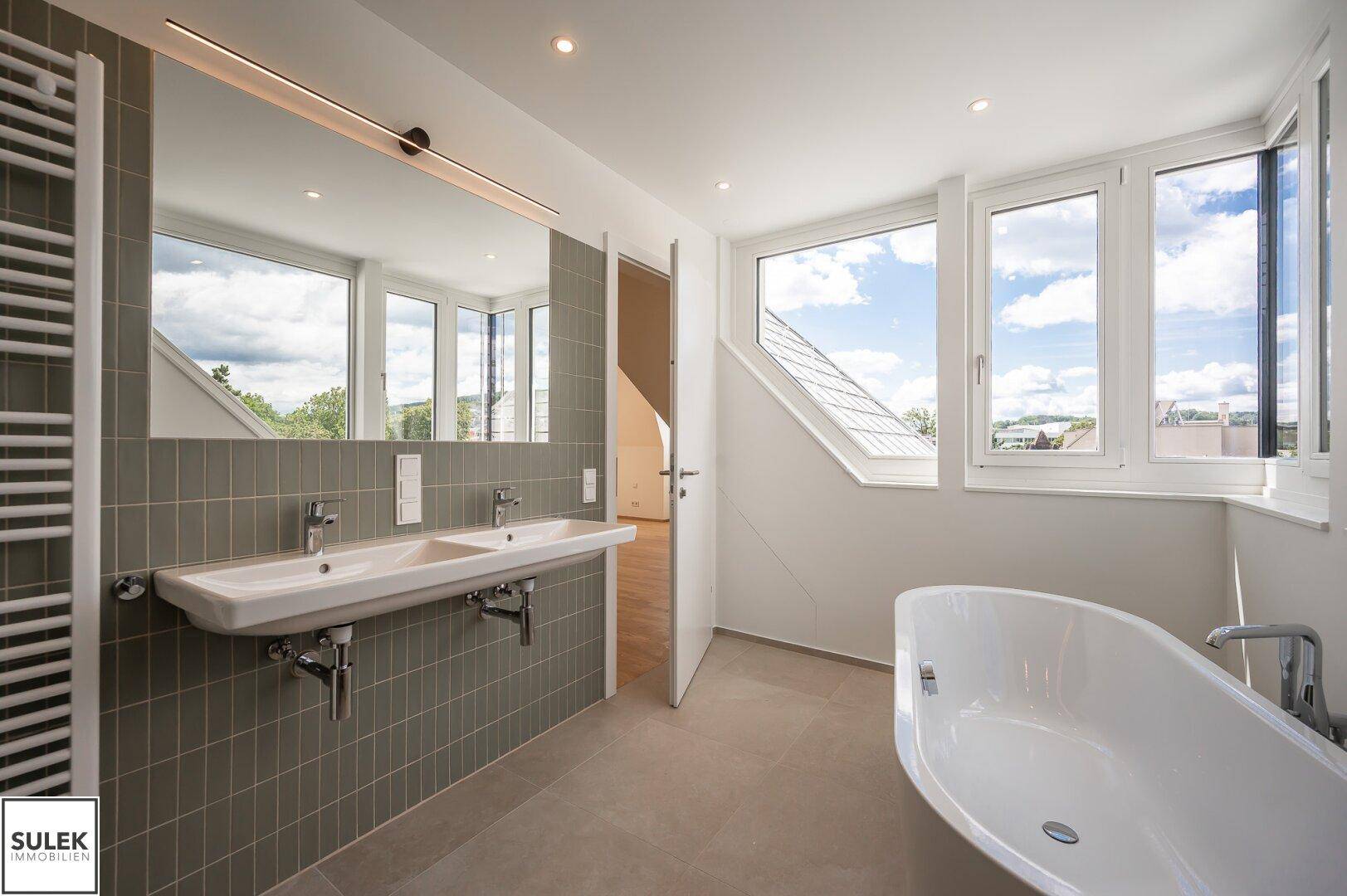 Modernes Badezimmer mit Doppelwaschbecken, freistehender Badewanne und großen Fenstern.