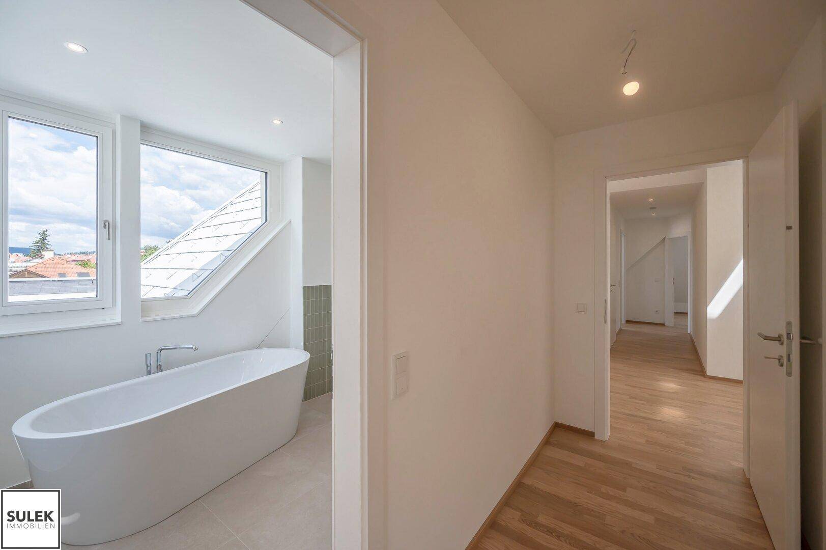 Heller Flur mit Holzboden und Zugang zu einem modernen Badezimmer mit Badewanne.