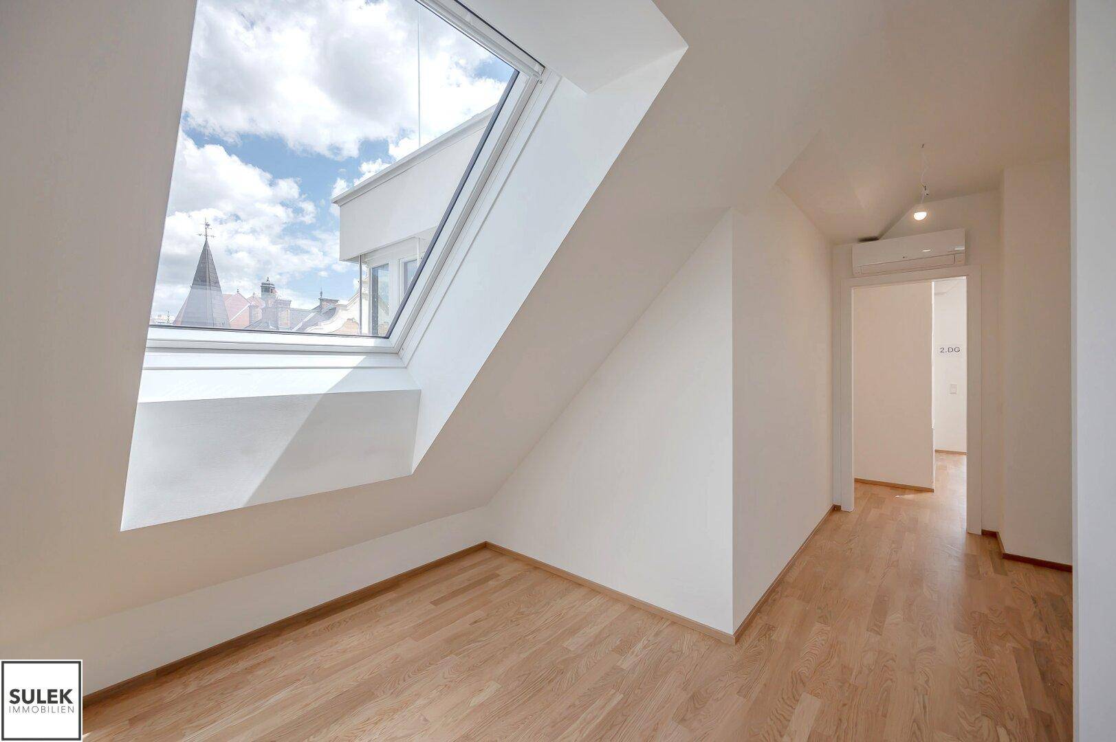 Helles Zimmer im Dachgeschoss mit Holzboden, großem Dachfenster und Klimaanlage.