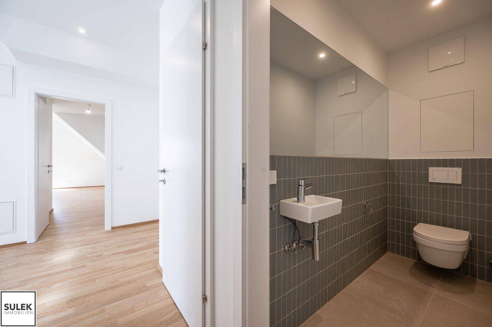 Modernes Gäste-WC mit kleinem Waschbecken, wandhängendem WC und grauen Fliesen.