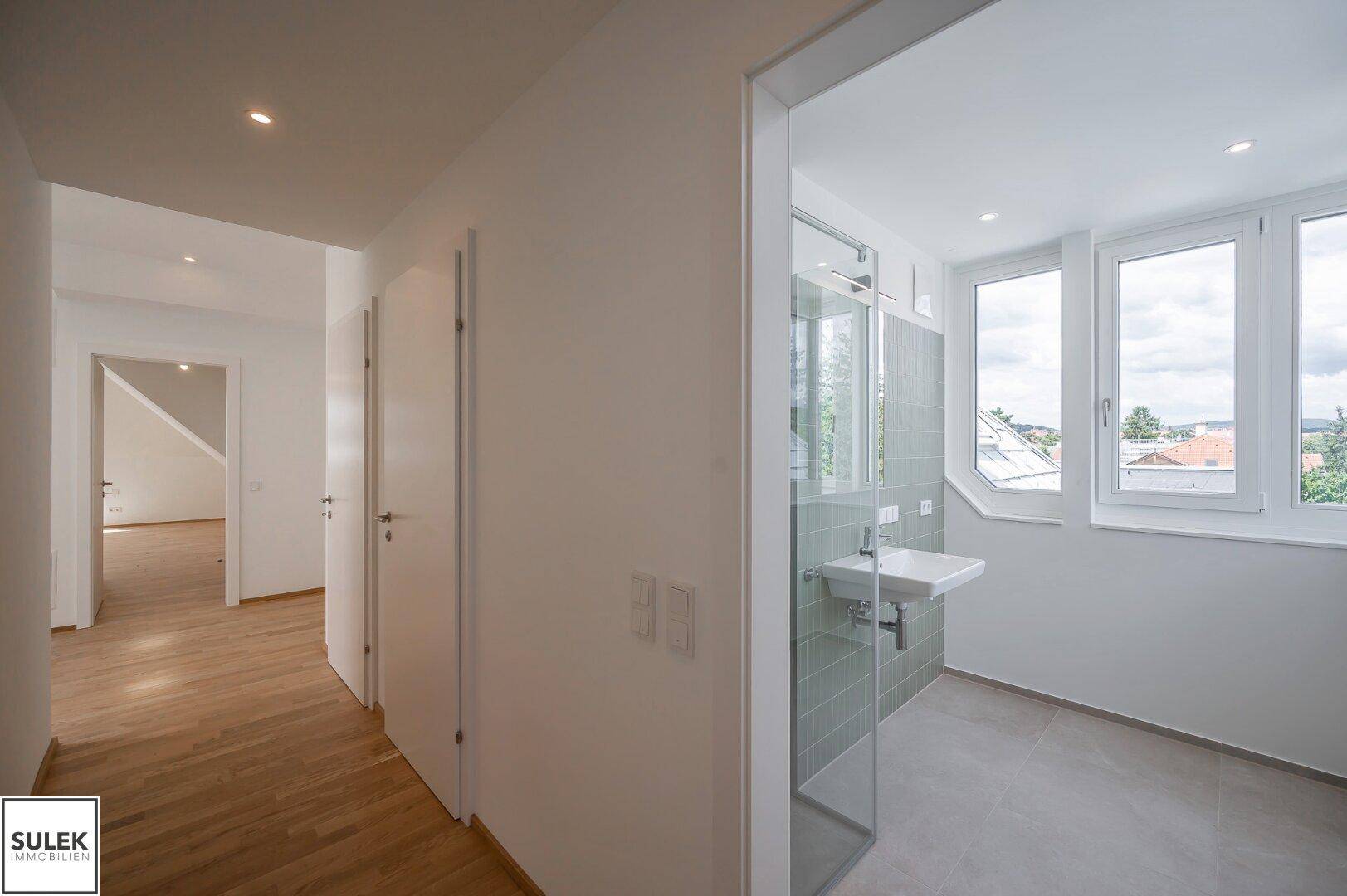 Heller Flur mit Holzboden und Blick in ein modernes Badezimmer mit Dusche.