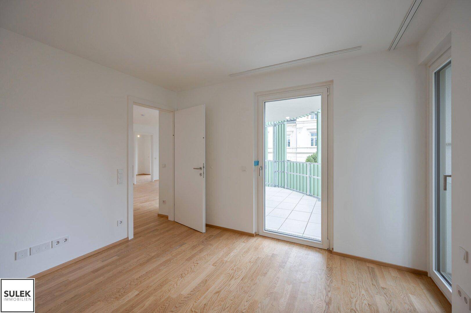 Helles Zimmer mit Parkettboden und direktem Zugang zu einem Balkon.