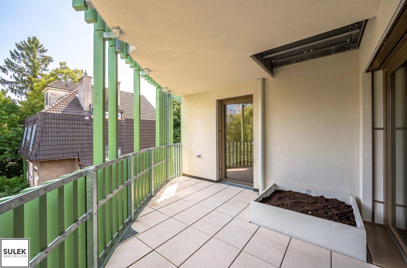 Sonniger Balkon mit grünen Lamellen, Fliesenboden und Blick auf die Umgebung.