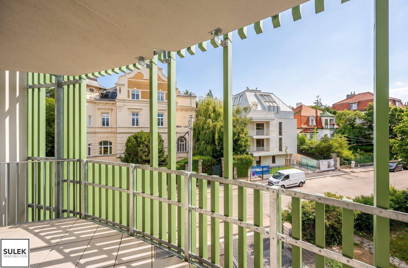 Breiter Balkon mit grünen Lamellen, Fliesenboden und Blick auf die Straße.