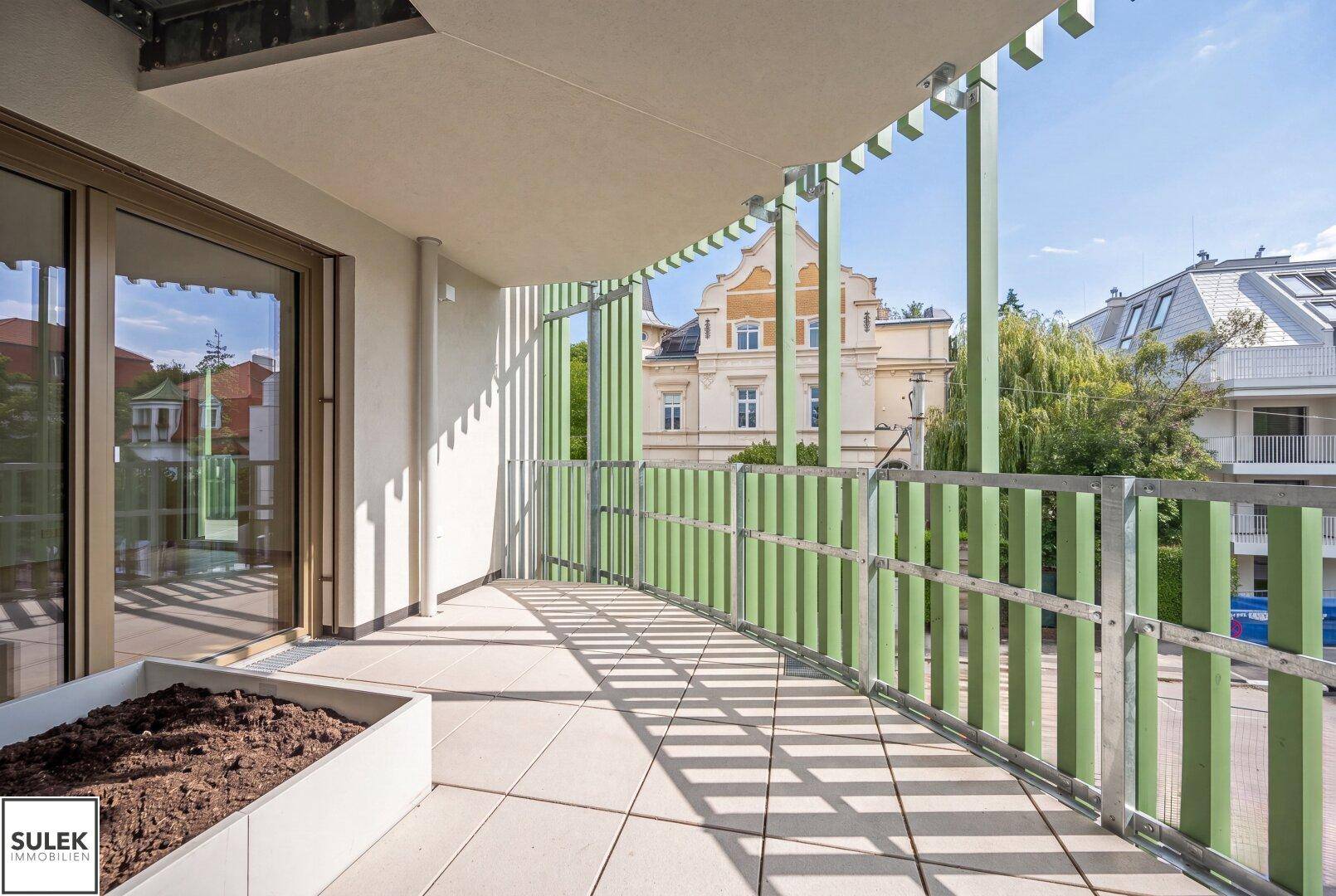 Geräumiger Balkon mit grünen Lamellen, Fliesenboden und einem Pflanztrog.