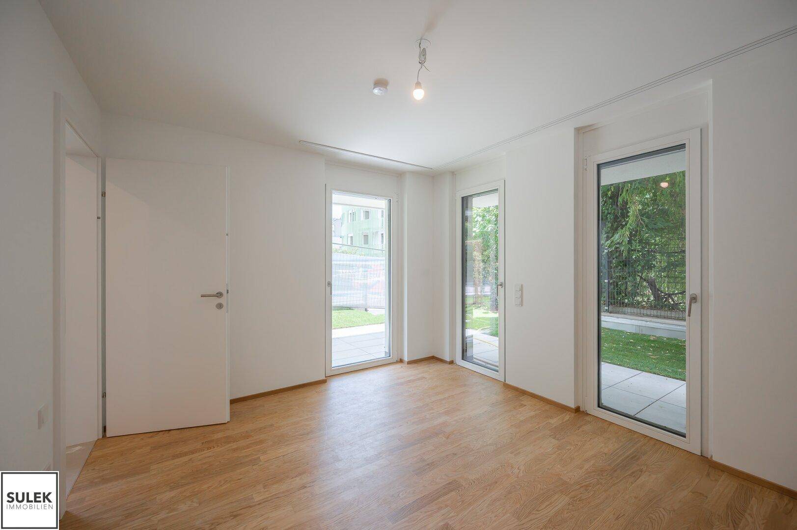 Lichtdurchfluteter Raum mit Parkettboden und mehreren Fenstertüren, die viel Helligkeit spenden.