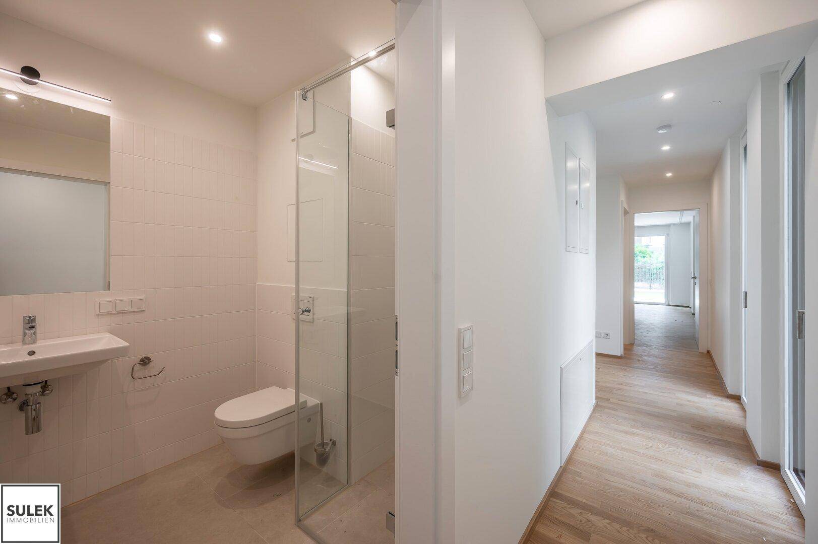 Modernes Badezimmer mit ebenerdiger Dusche, wandhängendem WC und elegantem Waschbecken.