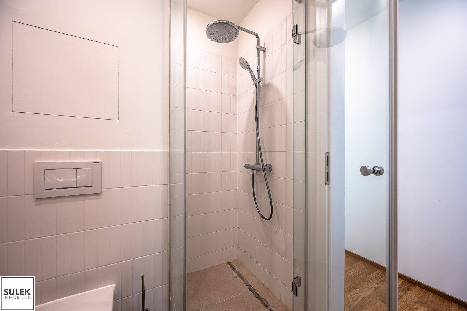 Detaillierte Ansicht einer modernen Glasdusche mit Regenduschkopf und Handbrause.