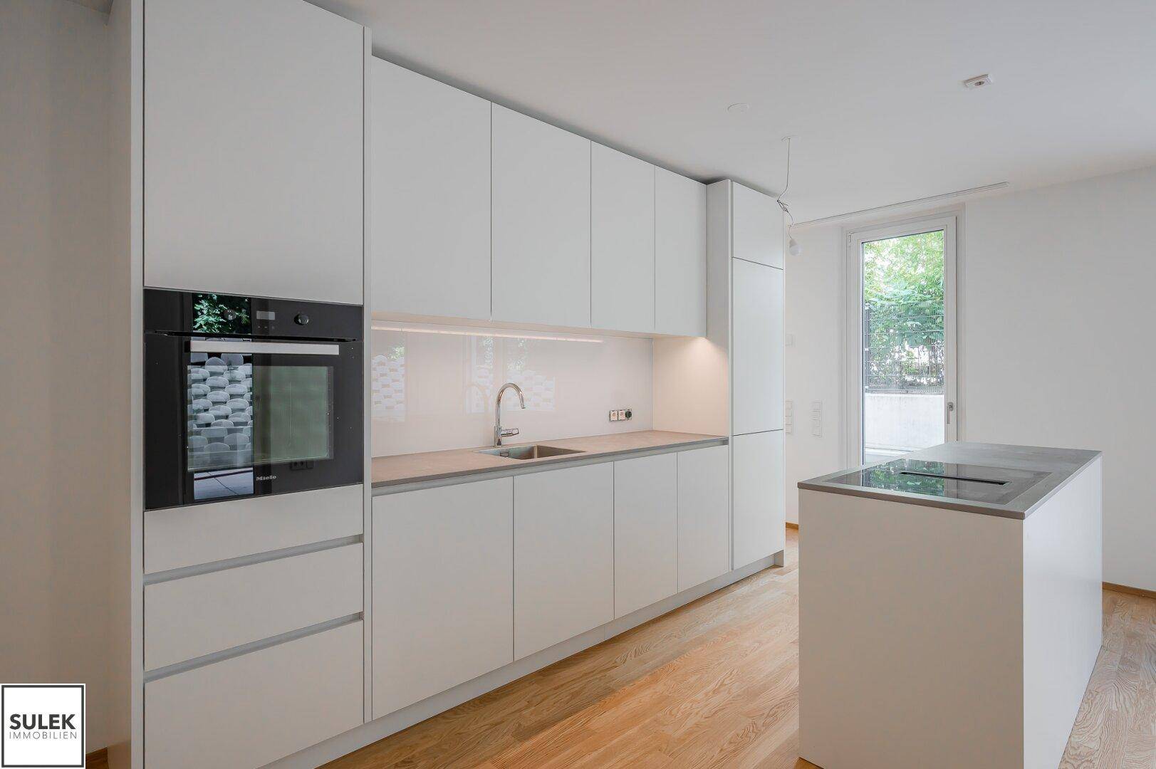 Moderne weiße Einbauküche mit integriertem Backofen, Spüle und Kochinsel.