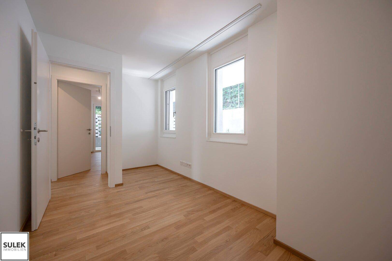 Heller Raum mit Parkettboden und zwei Fenstern, ideal als Schlaf- oder Arbeitszimmer.
