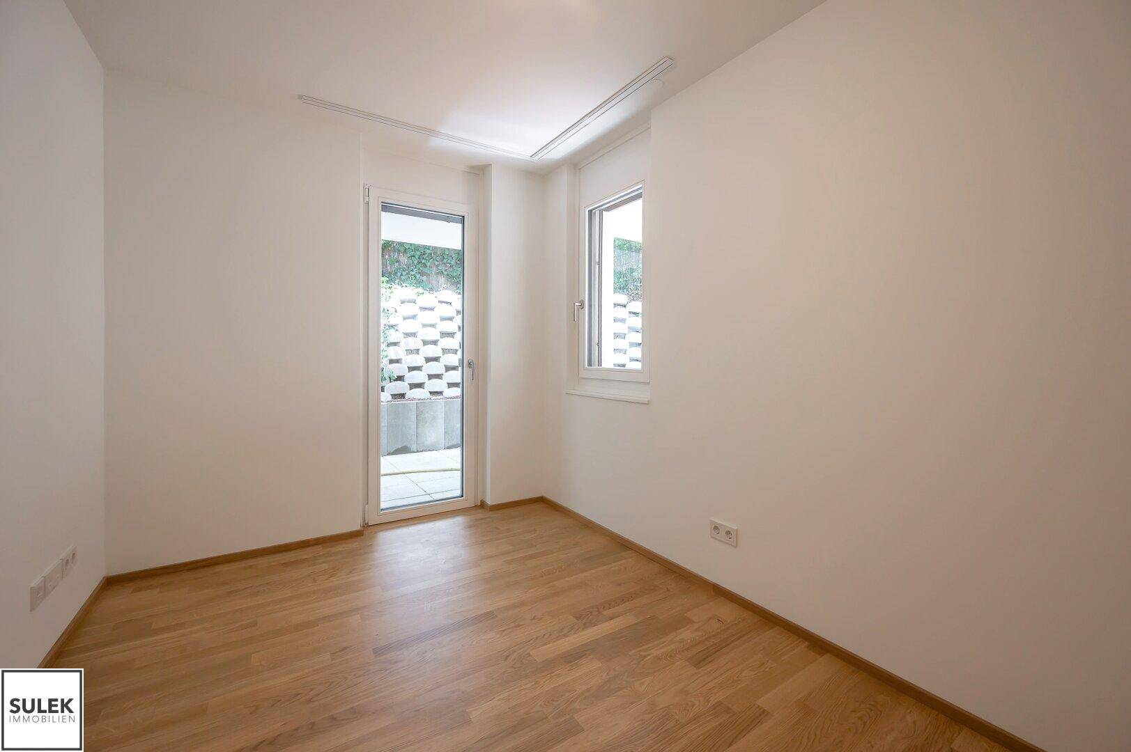 Leerer Raum mit Holzboden und Zugang zu einem Außenbereich, bietet viel Tageslicht.