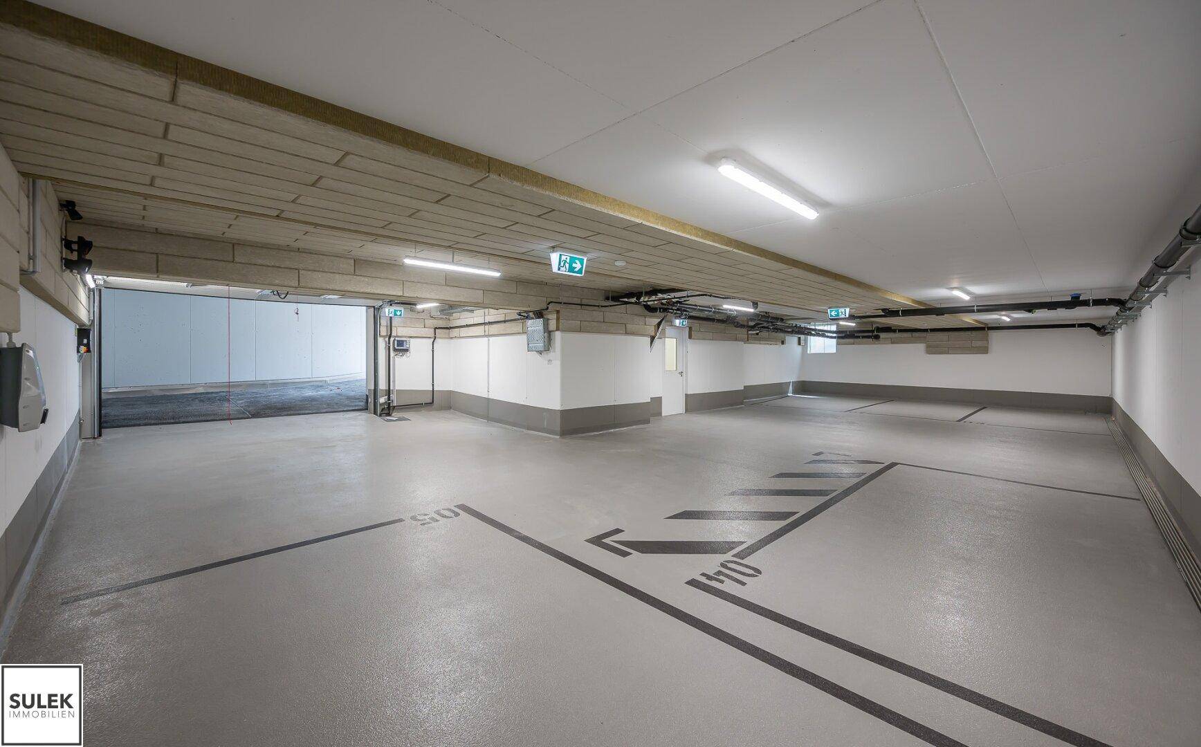 Geräumige und gut beleuchtete Tiefgarage mit markierten Stellplätzen.