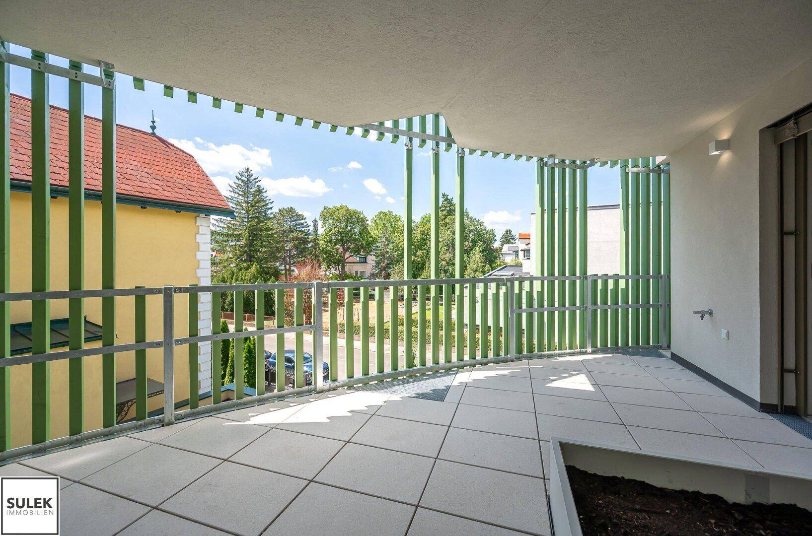Geräumiger Balkon mit Fliesenboden und grünen Sichtschutzelementen, bietet einen angenehmen Blick ins Grüne.
