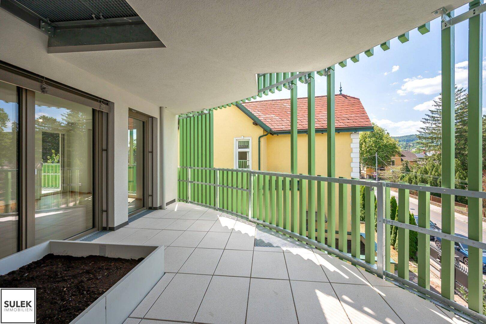 Breiter Balkon mit Fliesen und grünen Lamellen, ideal für Entspannung im Freien mit Blick auf die Umgebung.