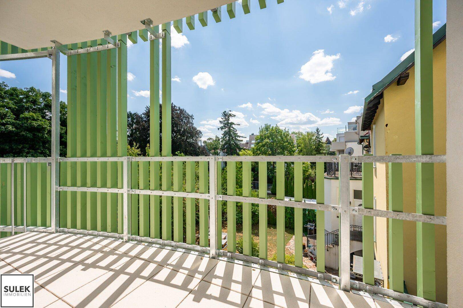 Heller Balkon mit Fliesenboden und grünen Sichtschutzelementen, bietet einen weiten Blick ins Grüne.