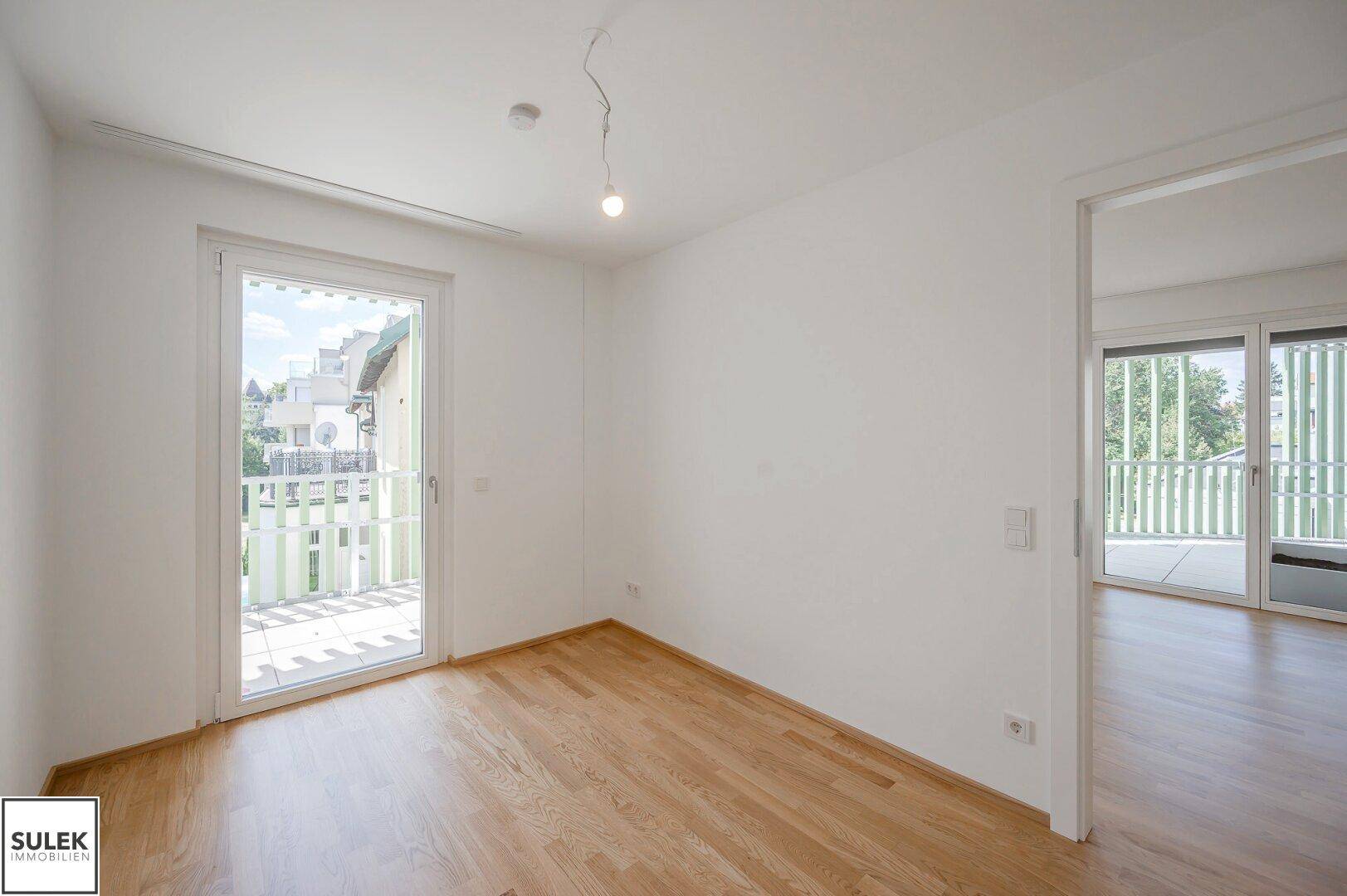 Helles Zimmer mit Parkettboden und Zugang zu einem Balkon, ideal als Schlaf- oder Arbeitszimmer.