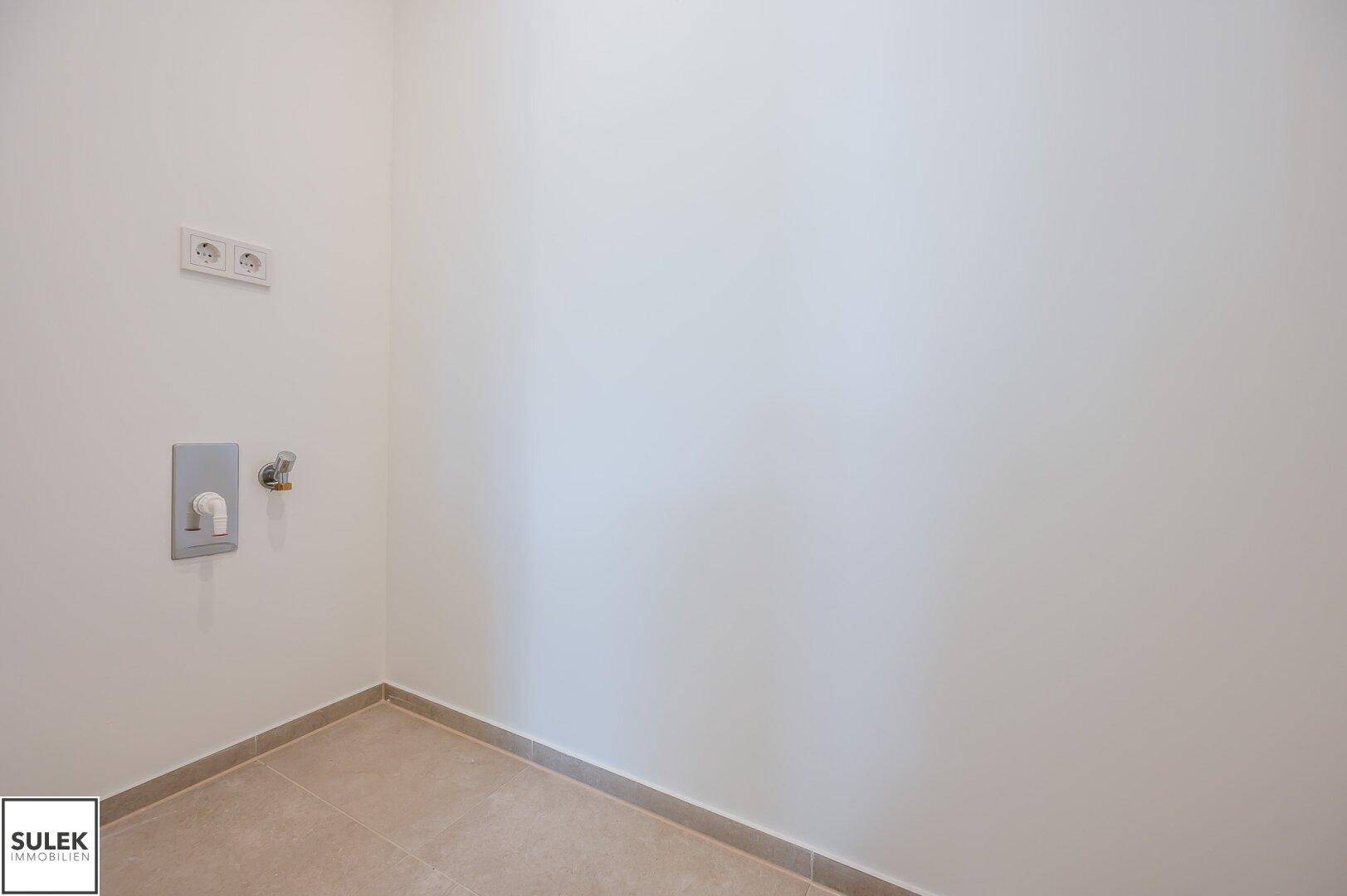 Leerer Hauswirtschaftsraum mit Fliesenboden und Anschlüssen für Waschmaschine und Trockner, bereit zur Nutzung.