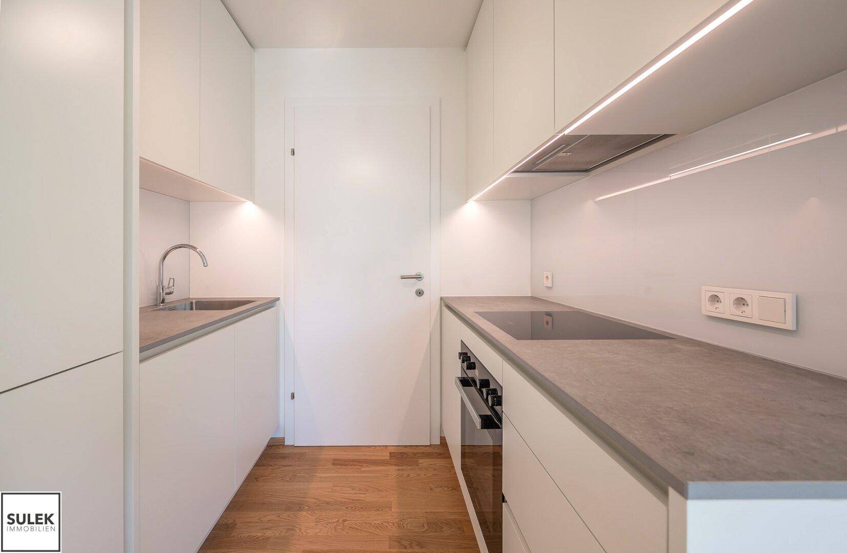 Moderne, kompakte Küche mit weißen Schränken, integrierten Geräten und Arbeitsplatte in Betonoptik.