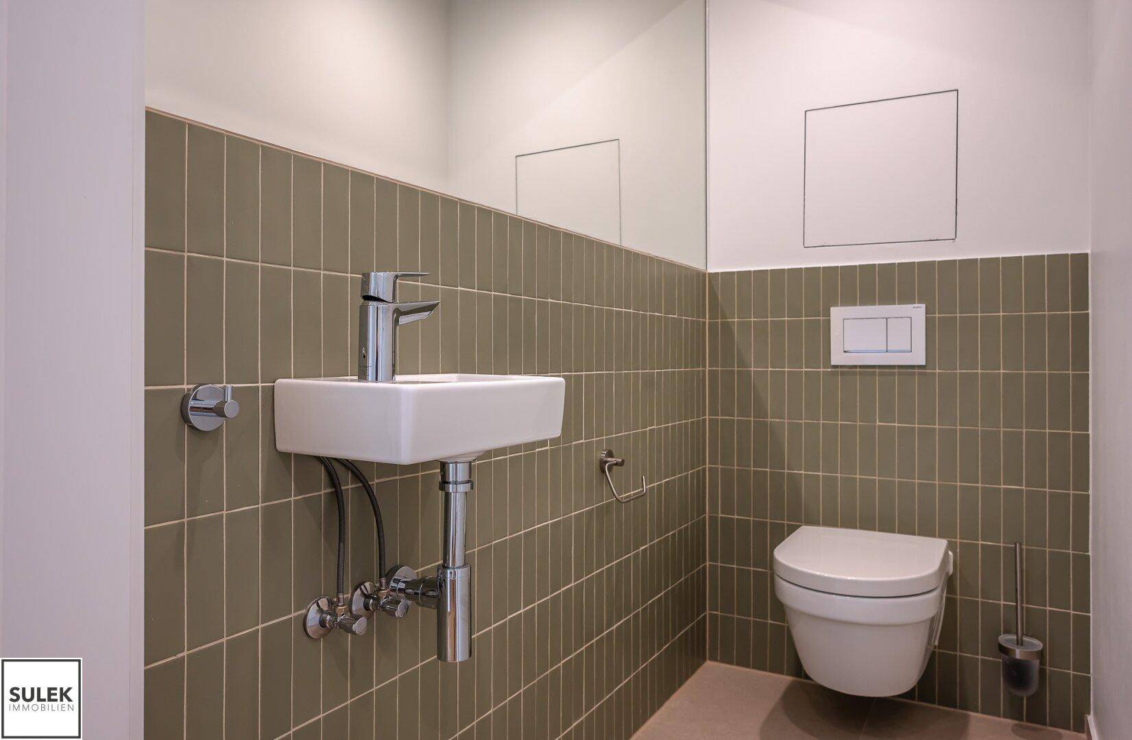 Modernes Gäste-WC mit Wand-WC, kleinem Waschbecken und grünen Fliesen an der Wand, sehr gepflegt.