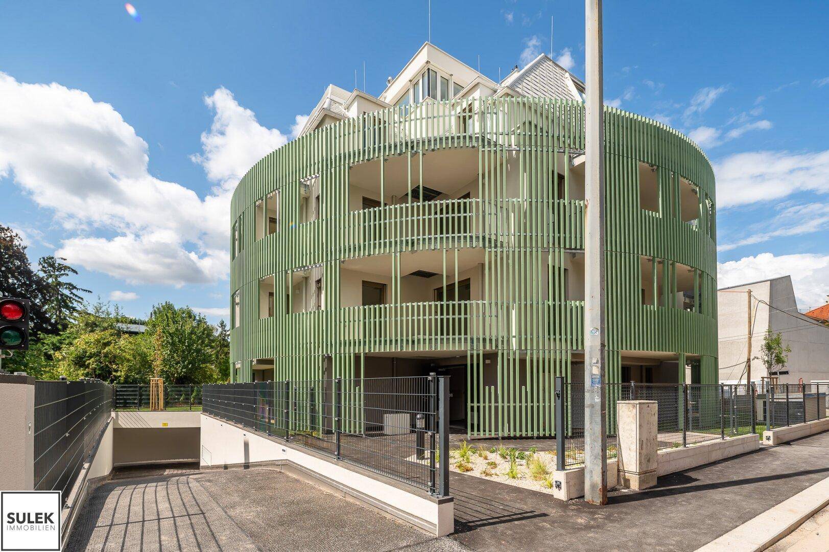 Moderne Wohnanlage mit markanter grüner Fassade und Tiefgaragenzufahrt.