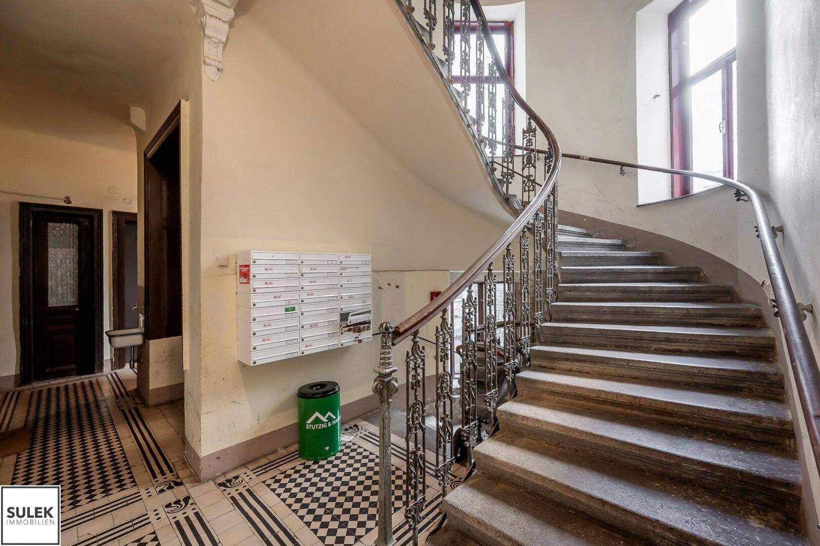 Historisches Treppenhaus mit schmiedeeisernem Geländer und gemustertem Fliesenboden.