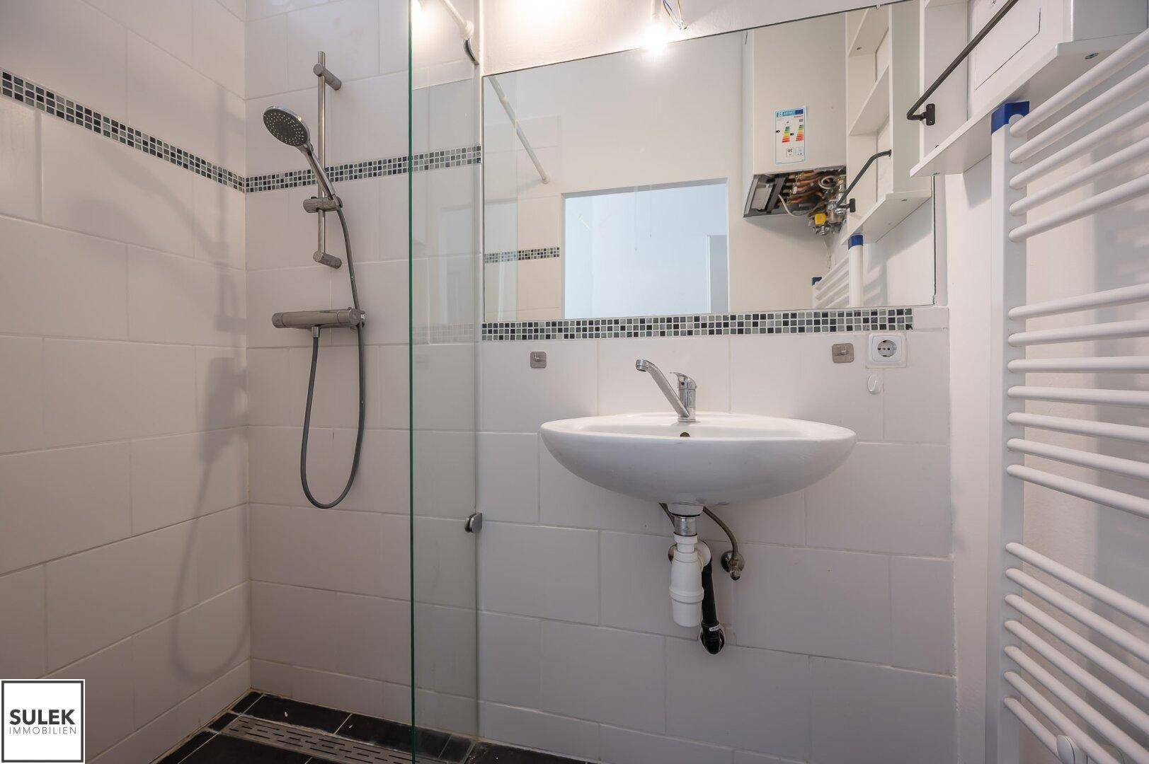 Badezimmer mit Duschkabine, Waschbecken und beheiztem Handtuchhalter, modern gefliest.