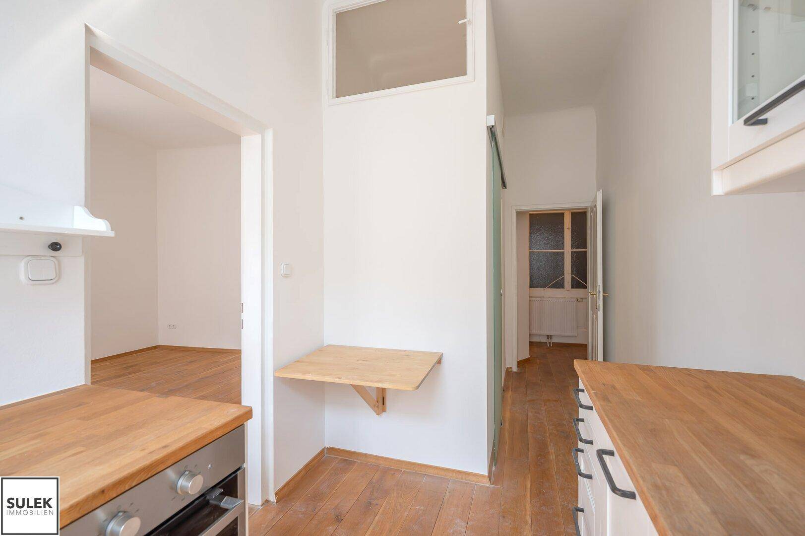 Küchenbereich mit Klapptisch und Zugang zu weiteren Räumen, ausgestattet mit Holzboden.